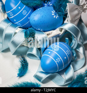 Easter background with blue eggs, feathers and ribbon in white basket. Square photo. Stock Photo