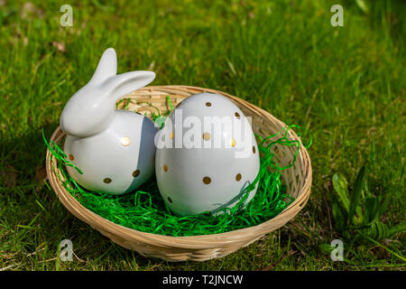 An Easter bunny and an Easter egg made of white pottery with golden polka dots in a basket on a meadow. Stock Photo