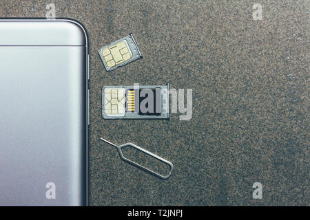 mobile phone and open slots for nano SIM cards, micro SD drive and metal key on grey background with copy space Stock Photo
