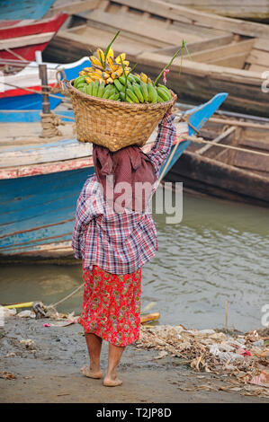 Woman carrying a basket of bananas on the banks of the Irrawaddy River, Mandalay, Myanmar (Burma) Stock Photo