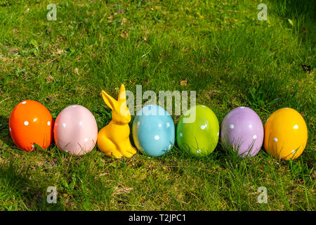 Colorful ceramic easter eggs and an Easter bunny in a line on a meadow. Stock Photo
