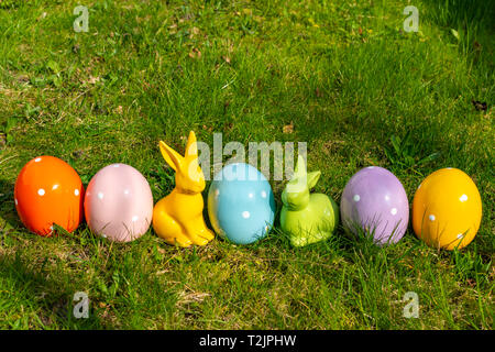 Colorful ceramic easter eggs and Easter bunnies in a line on a meadow. Stock Photo