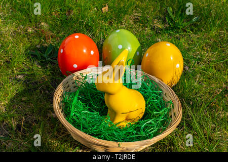 A yellow Easter bunny and colorful Easter eggs made of pottery with a basket on a meadow. Stock Photo