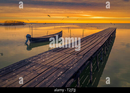 Lake scene in the morning at sunrise with birds flying above the lake and a boat and a pontoon in the foreground shot in Romania Stock Photo
