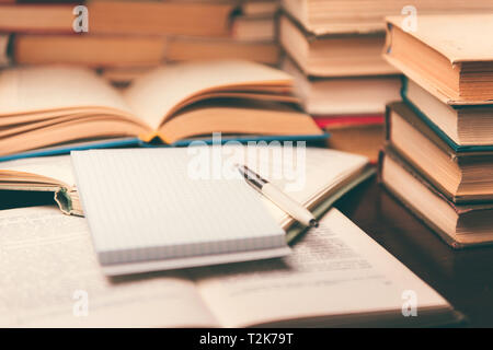 Education learning concept with open book and notebook on the table. Stack piles of books on reading desk and glasses in bookshelves background Stock Photo