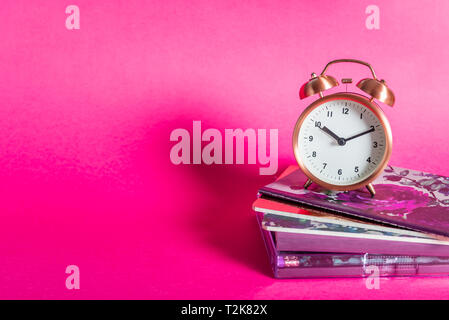 Different Notebooks and alarm clock on bright pink background. Idea of Girly Desk table or Office settings. Back to school concept Stock Photo