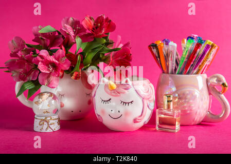 Unicorn mugs with Alstroemeria Flowers and flamingo mug with colorful gel pens on bright pink background. Idea of Girly Desk table or Office settings. Stock Photo