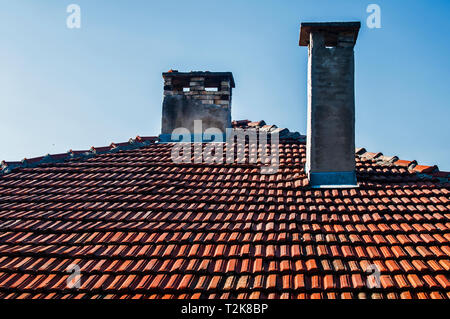Tiled house roof with two weathered chimneys on blue sky background Stock Photo