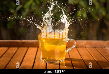 Splash of cool fresh tea with lemon in the transparent glass cup in the table outdoors Stock Photo