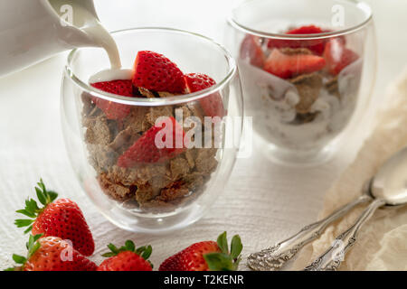 Toasted Bran Flakes Cereal with Yogurt and Fresh Strawberries in a Glass Cups on a Kitchen Table in White Background Stock Photo