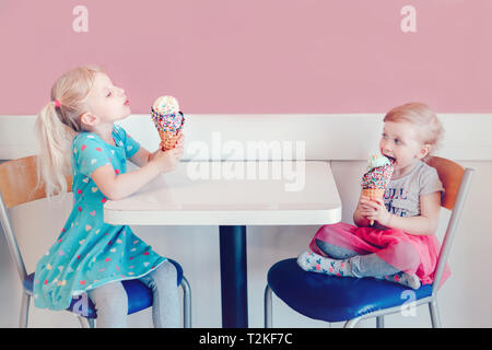 Lifestyle portrait of two happy Caucasian cute adorable funny children girls sitting together bragging boasting their ice-cream. Love envy jealous sis Stock Photo