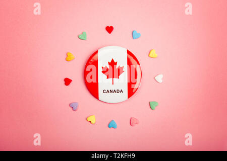 Happy Canada Day greeting card with Canadian flag in centre middle and many colorful candies hearts around it on living coral pink background. Stock Photo