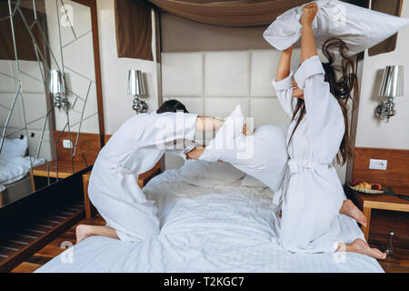 Cheerful couple have fun in the bedroom fighting with big pillows at home or hotel, staying in bed for all day Stock Photo