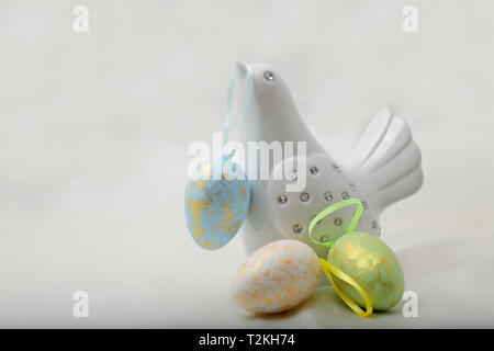 A white decorative bird with colourful Easter eggs. One hanging on its beak. Stock Photo