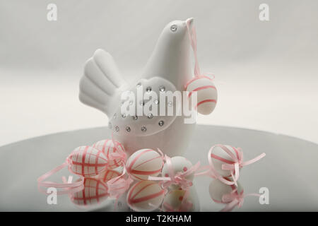 A white decorative bird with colourful Easter eggs. One hanging on its beak. Stock Photo