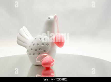 A white decorative bird with colourful Easter eggs. One hanging on its beak. Stock Photo