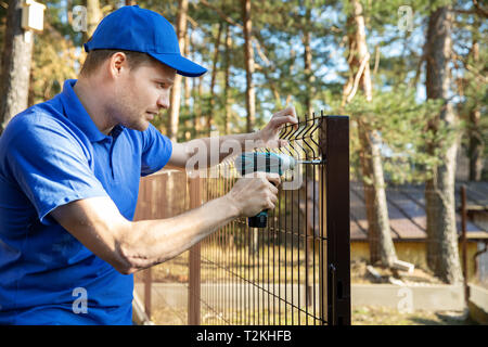 fencing services - worker installing welded metal mesh fence Stock Photo