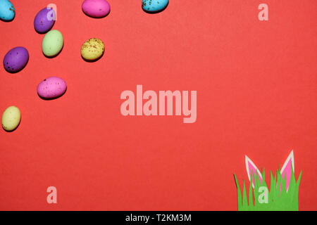 Speckled Candy Eggs With Rabbit Ears And Grass On Red Stock Photo