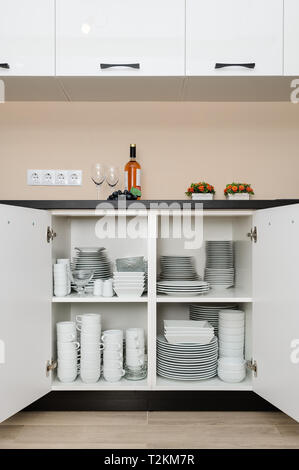 Dishware storage cabinet with open doors, white plates, bowls cups and other china crockery inside, front view Stock Photo