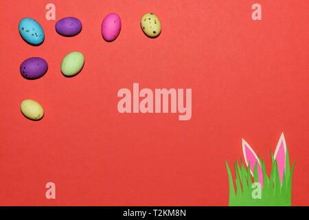Candy Eggs With Grass Patch And Rabbit Ears On Red Stock Photo