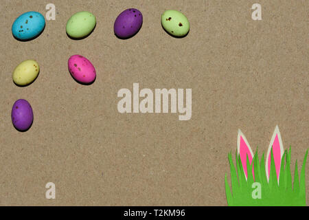 Candy Eggs With Grass Patch And Rabbit Ears On Natural Cardboard Stock Photo