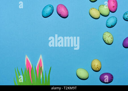 Candy Eggs On Blue With Grass Patch And Rabbit Ears Stock Photo