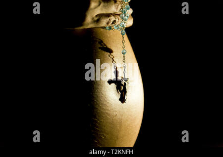Pregnant with hands on belly and rosary, praying. Stock Photo