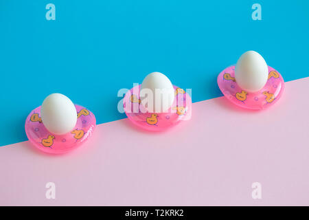 Three eggs in swimming pool floats abstract on colorful background. Stock Photo