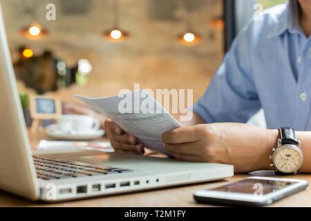Businessman using laptop while looking at invoice Stock Photo