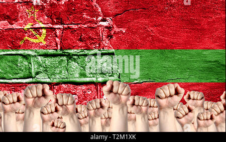 Male hands clenched in a fist raised up against the backdrop of a destroyed brick wall with a flag of Transnistria. The concept of the labor movement  Stock Photo