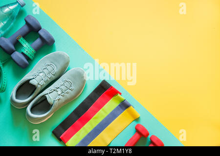 Sport and fitness equipment, rubber band, dumbbells, fitness shoes, measuring tape on punchy yellow. View from above, space for text. Stock Photo