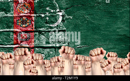 Male hands clenched in a fist raised up against the backdrop of a destroyed brick wall with a flag of Turkmenistan. The concept of the labor movement  Stock Photo