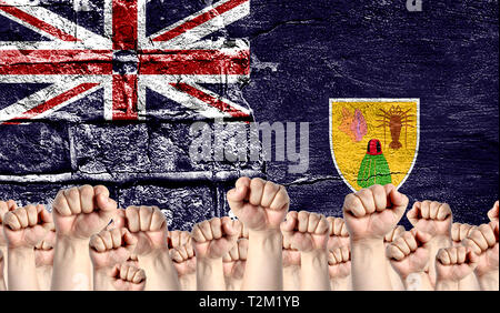 Male hands clenched in a fist raised up against the backdrop of a destroyed brick wall with a flag of Turks and Caicos Islands. The concept of the lab Stock Photo