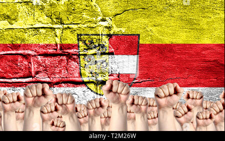 Male hands clenched in a fist raised up against the backdrop of a destroyed brick wall with a flag of Carinthia. The concept of the labor movement fro Stock Photo