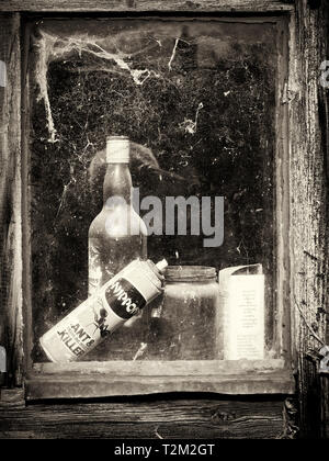 A glimpse through the window of an old garden shed with abandoned bottles and cans seen through cobweb covered glass. Stock Photo