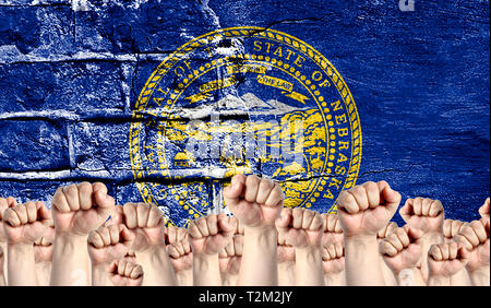 Male hands clenched in a fist raised up against the backdrop of a destroyed brick wall with a flag State of Nebraska. The concept of the labor movemen Stock Photo