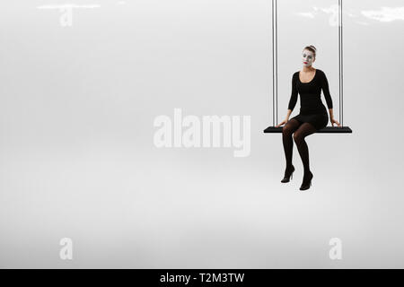 Woman mime in black suit sitting on swing. Mixed media Stock Photo