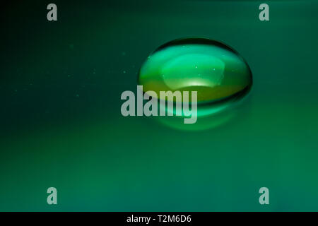 Macro photograph of a drop of green water or a liquid with bubbles on a smooth and reflective surface Stock Photo