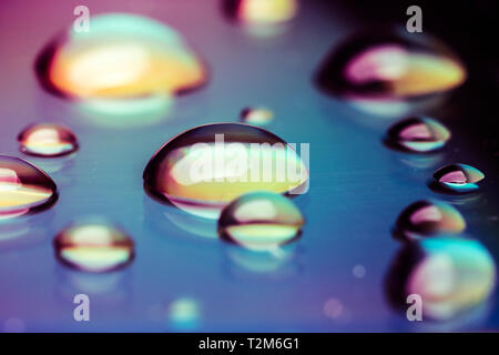 Macro close-up of a group of liquid rainbow colored water drops, on shiny surface, abstract background Stock Photo