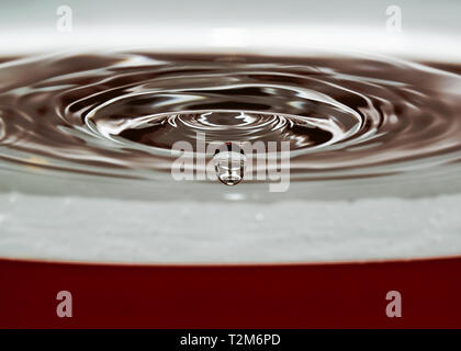 A drop of water impacts the surface forming circular waves Stock Photo
