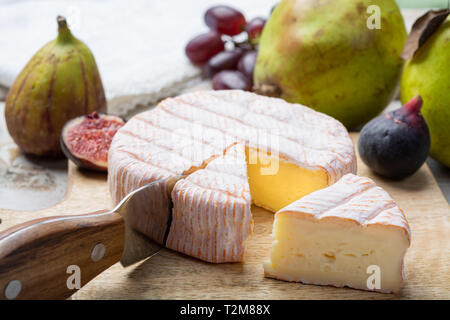 Round piece of French cheese Fleur Rouge made from cow milk served as dessert with fresh figs and pears close up Stock Photo