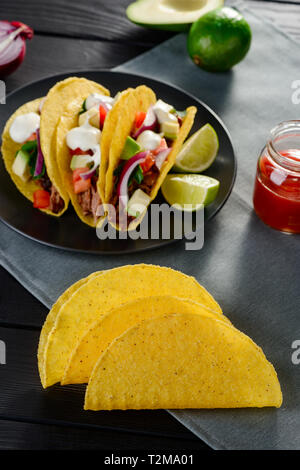 Tacos and corn tortillas on a kitchen table. Filling with avocado, beef, vegetables and sour cream. Cooking tasty Mexican food at home. Stock Photo
