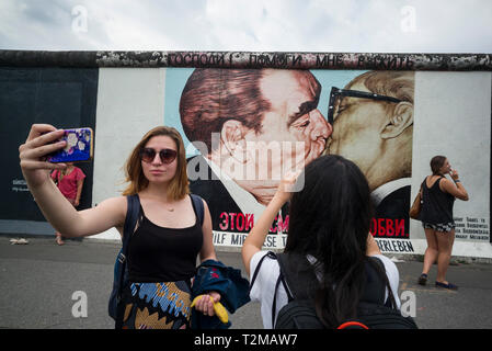 Berlin. Germany. Tourists pose for photos infront of one of the remaining sections of the Berlin Wall at the East Side Gallery.   Tourists pose for ph