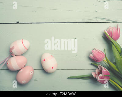 Three beautiful pink tulips with Easter eggs on a rustic wooden background with space for text, spring or holidays background Stock Photo
