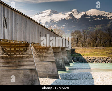 old wooden covered bridge crossing the Rhine river from Liechtenstein to Switzerland with a great view of the Swiss Alps in spring under a blue sky Stock Photo