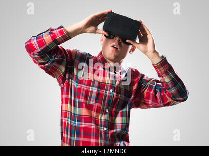 Young man in checked shirt wearing virtual helmet against gray background Stock Photo