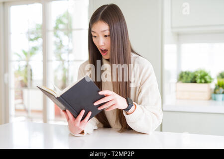 Beautiful Asian woman reading a book scared in shock with a surprise face, afraid and excited with fear expression Stock Photo
