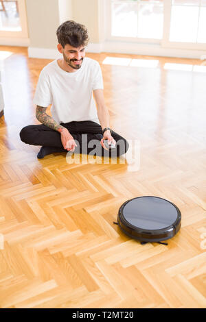 Young man using automatic vacuum cleaner to clean the floor, controling machine housework robot Stock Photo