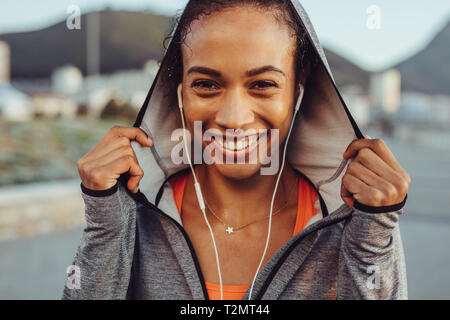 Close up of smiling young woman wearing sportswear and earphone. Confident fitness woman in a hoodie. Stock Photo