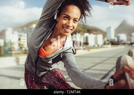 Fitness female doing leg stretches outdoors. Woman athlete working out on a railing by the road. Stock Photo